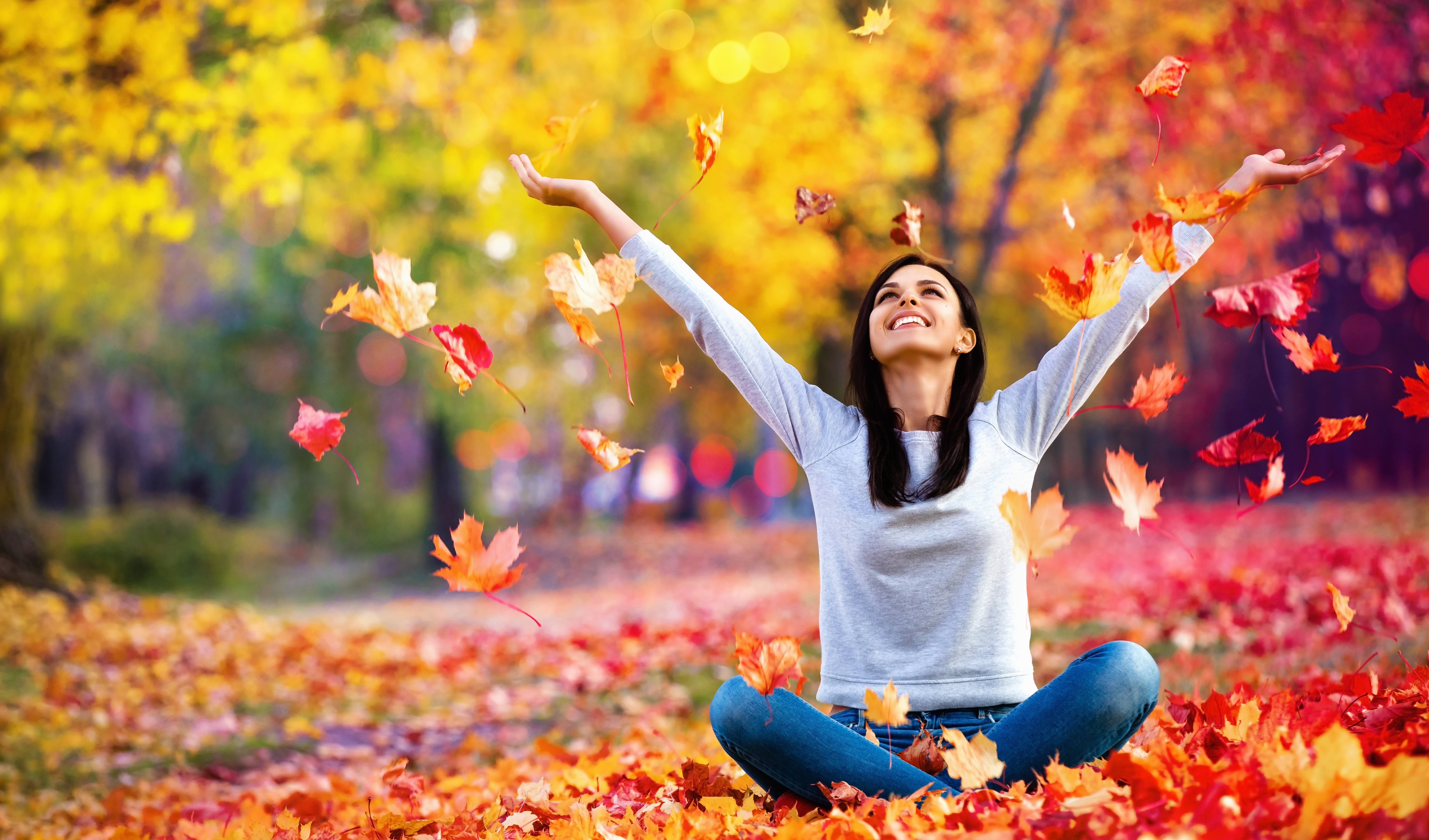 woman sitting in a pile of leaves tossing them in the air