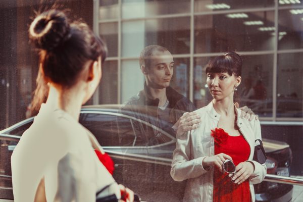 Pretty woman is looking at the show-window. Her dead beloved is embracing her in the reflection.